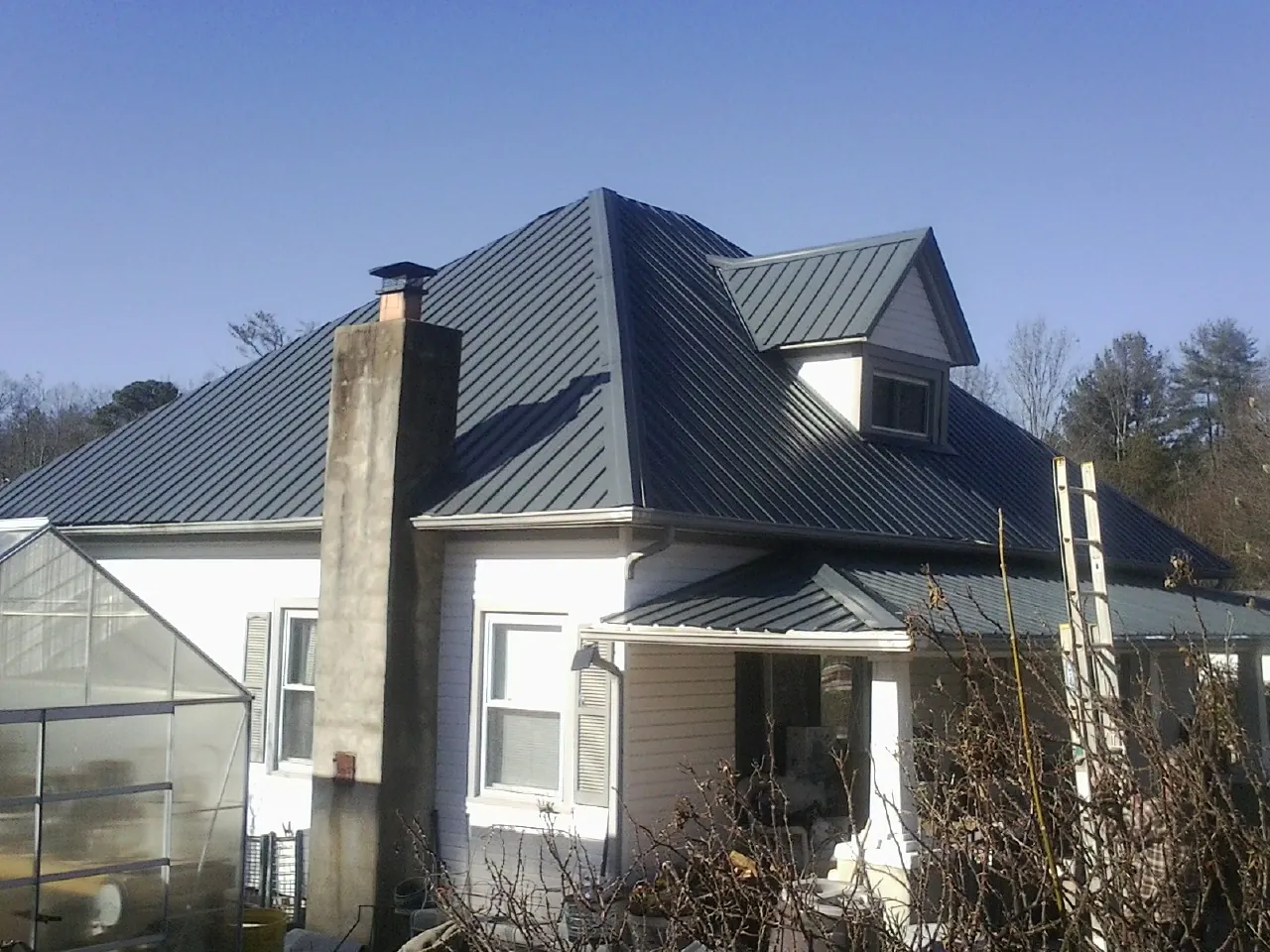Dark blue standing seam metal roof on a white farmhouse with dormer — Slate & Tile Roof Repair by Roofing Brothers in Plantersville