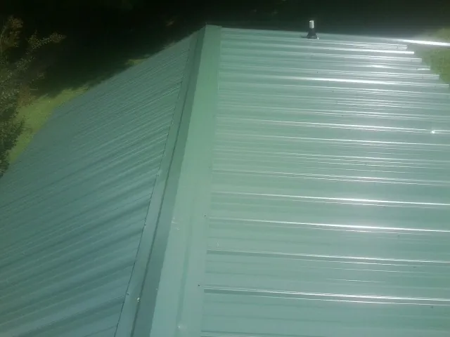 New green metal panels meeting at the ridge of a roof — Flat Roof Repair work by our crew in Plantersville