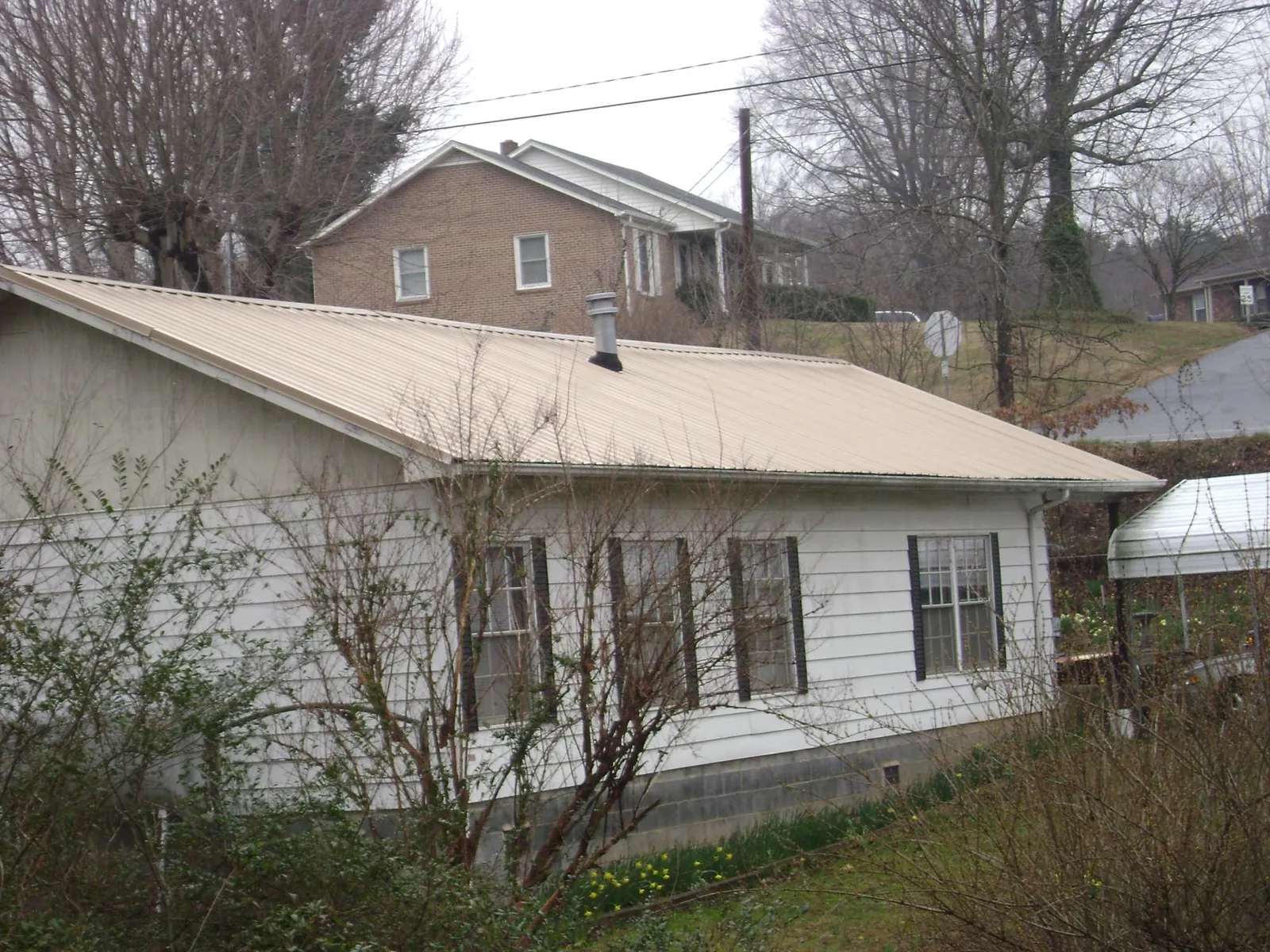 Tan metal roof on a white sided house set into a hillside — Commercial Roofing by Roofing Brothers in Plantersville